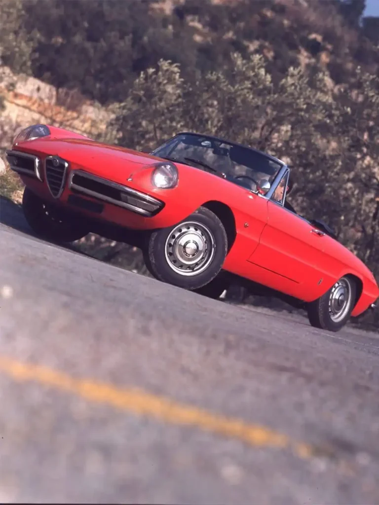 red vintage Alfa Romeo Spider "Duetto" driving on a road.